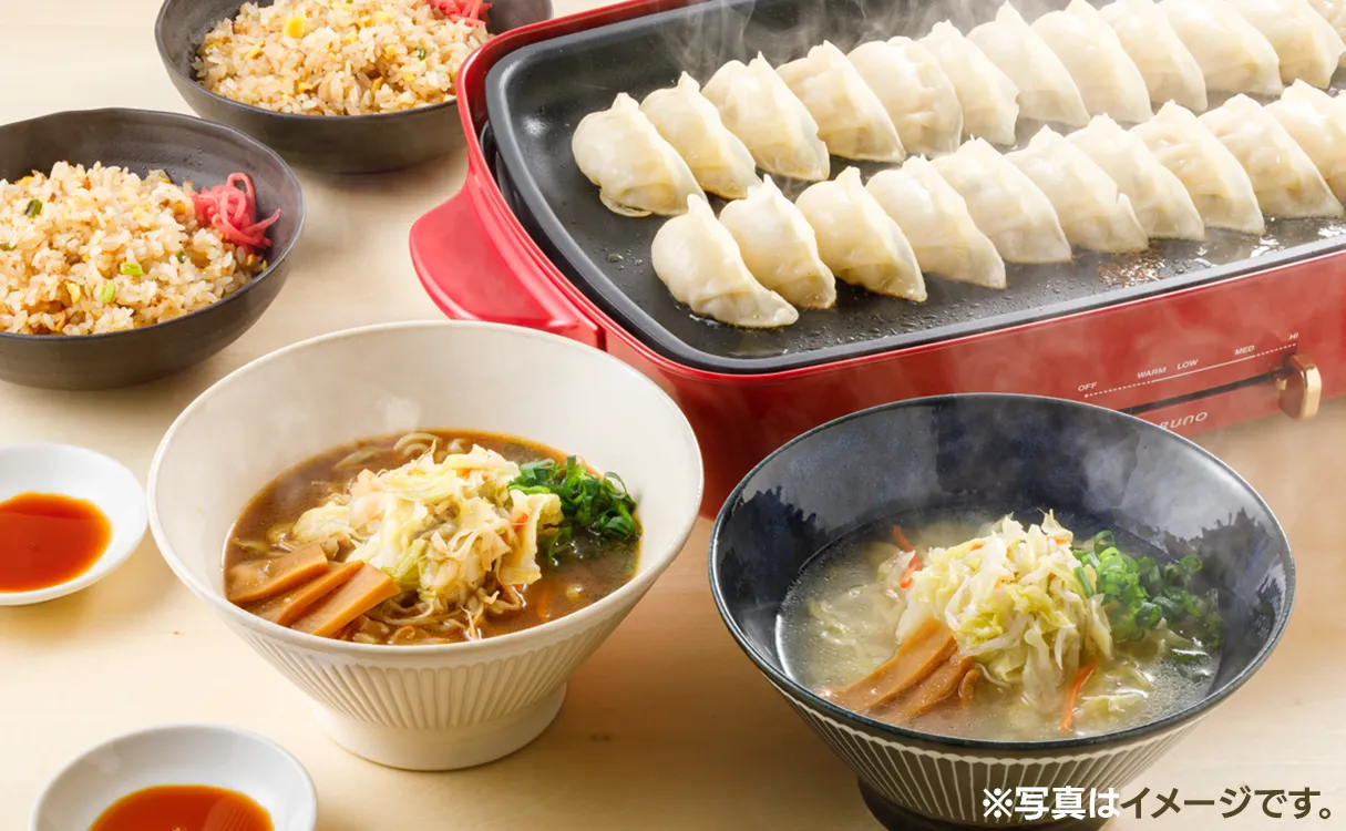 セット内容の調理イメージ。食卓にチャーハン、ラーメンの盛り付けられた器とホットプレートで焼いている餃子の写真です。